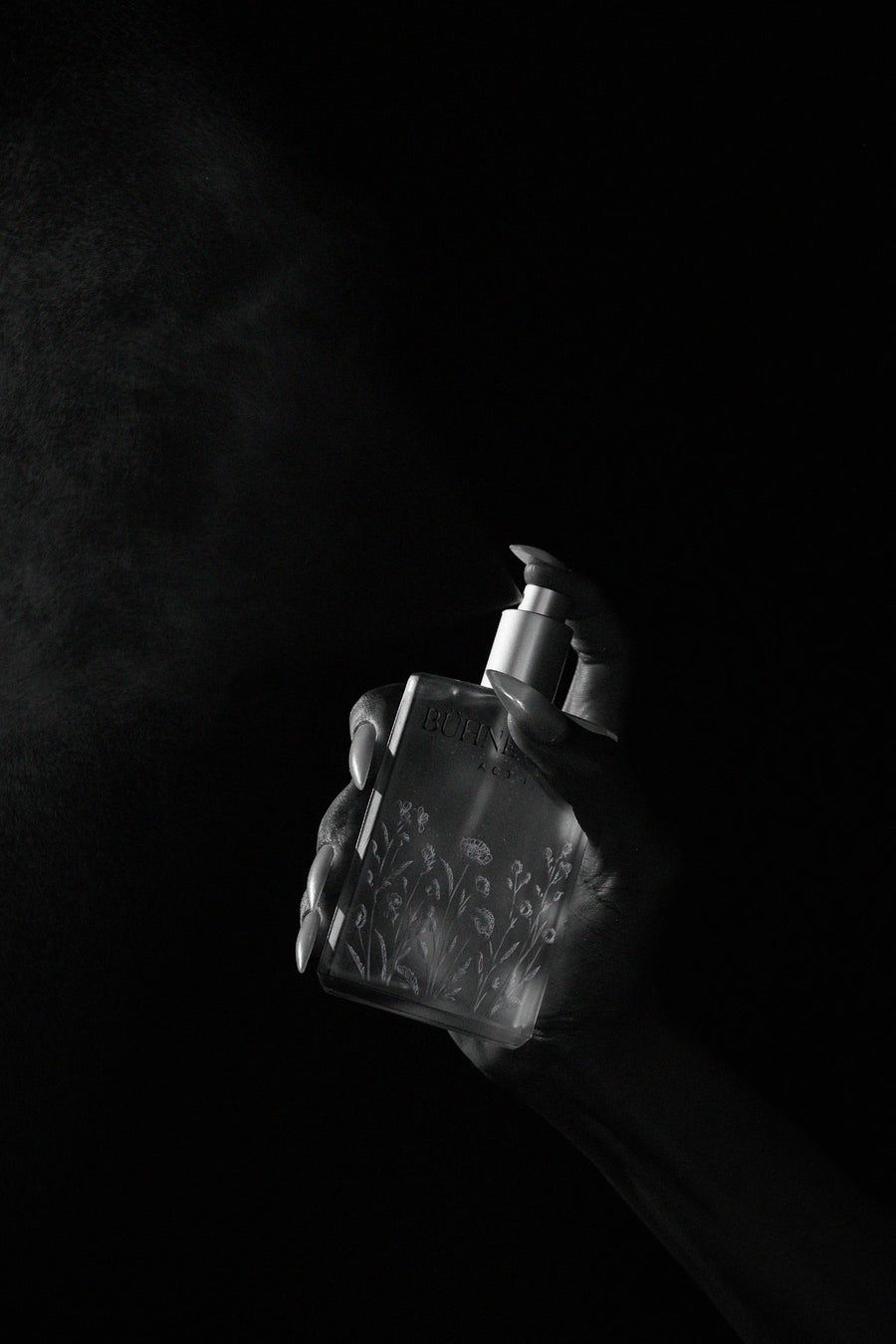 A hand holding BÜHNE NOIR Act I Body Elixir in dramatic black and white